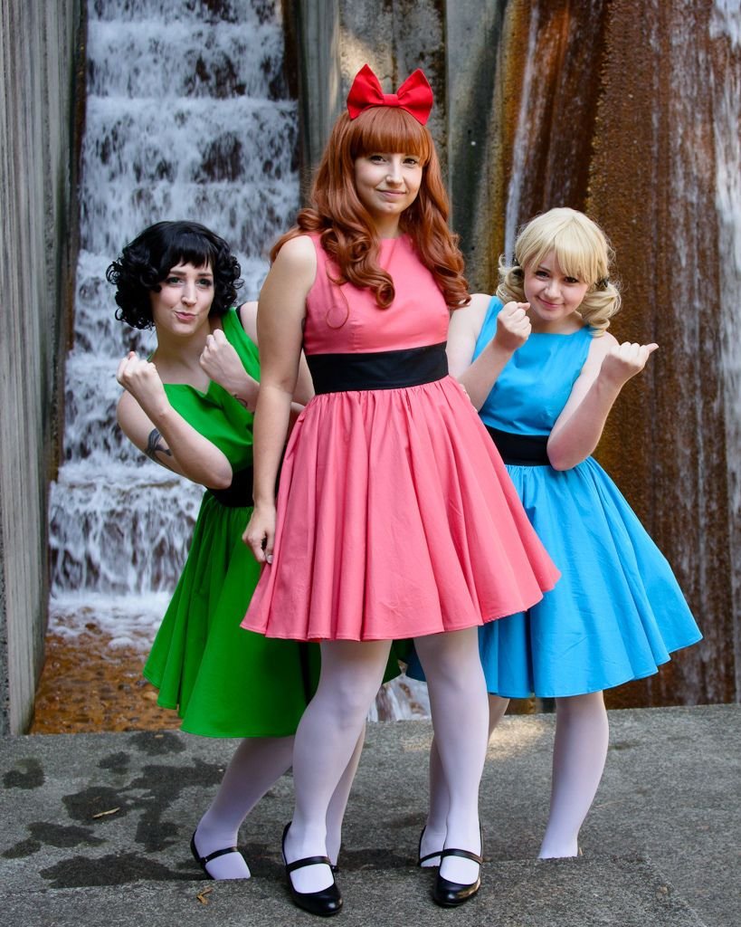 Three women dressed as the Powerpuff Girls in pink, blue, and green dresses for Halloween