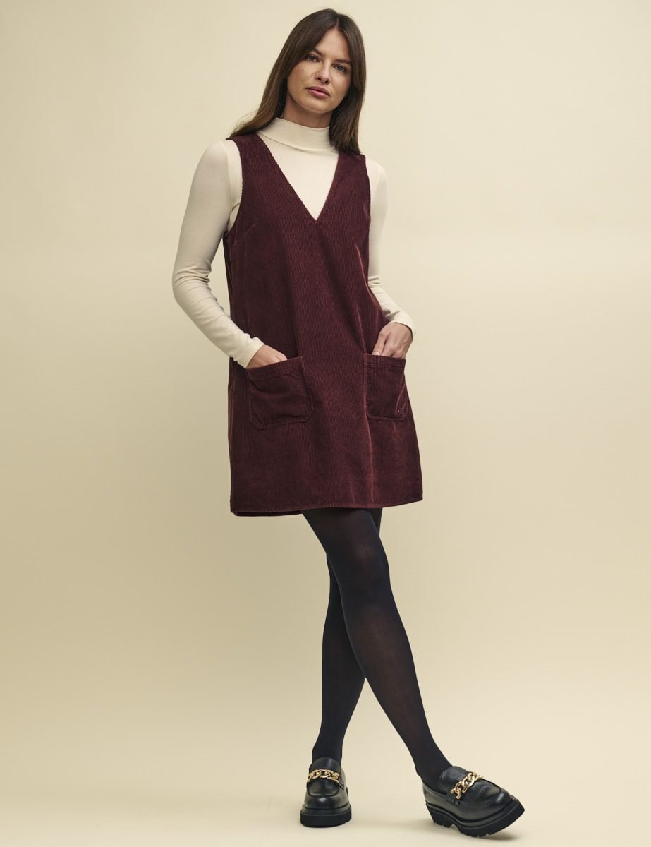 Woman wearing a burgundy corduroy pinafore dress with turtleneck