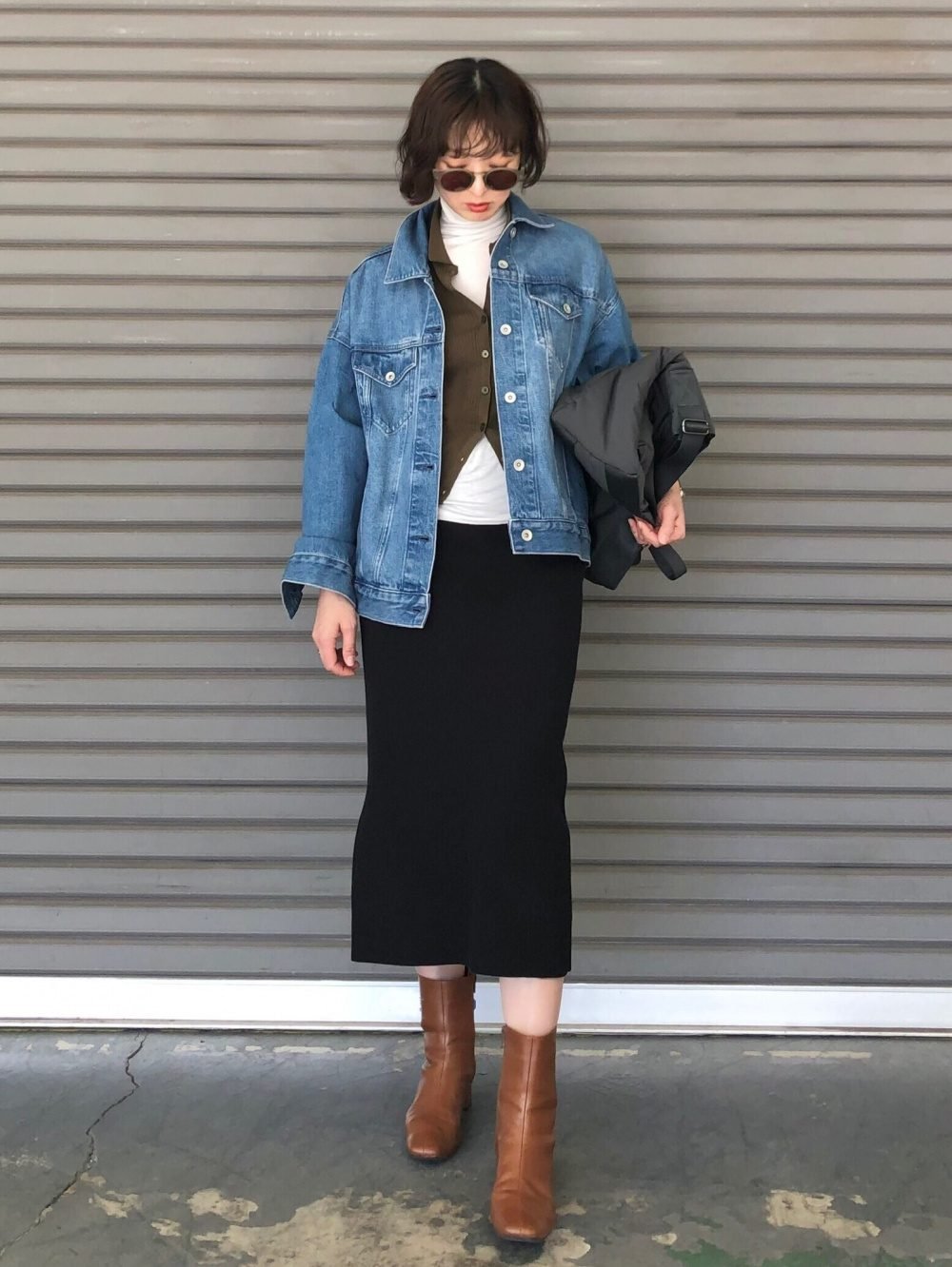 Woman wearing denim jacket layered over cardigan with midi boots