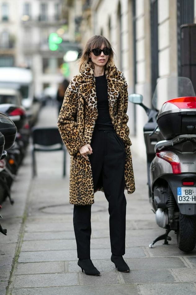 Woman wearing leopard faux fur coat over all-black outfit with boots