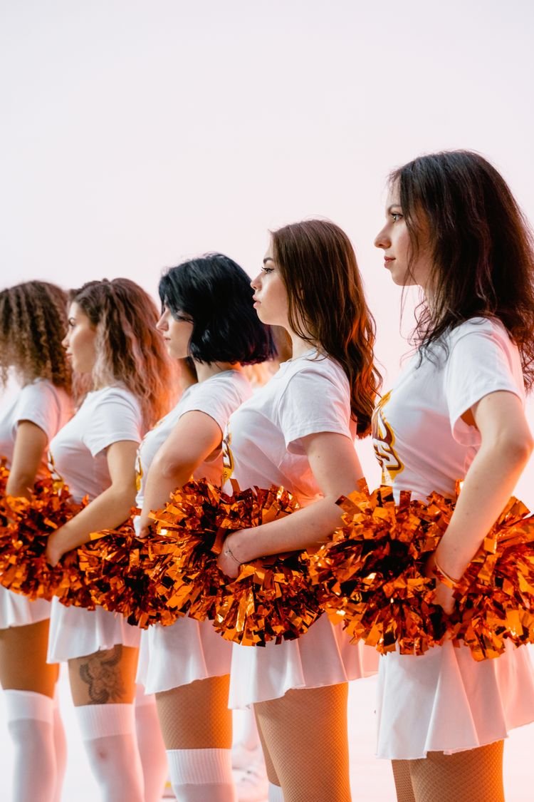 Woman wearing a cheerleader 00s Halloween costume with pom poms