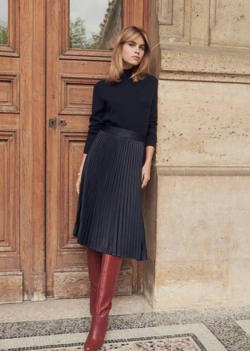 Woman wearing a pleated midi skirt with a black turtleneck and knee-high boots