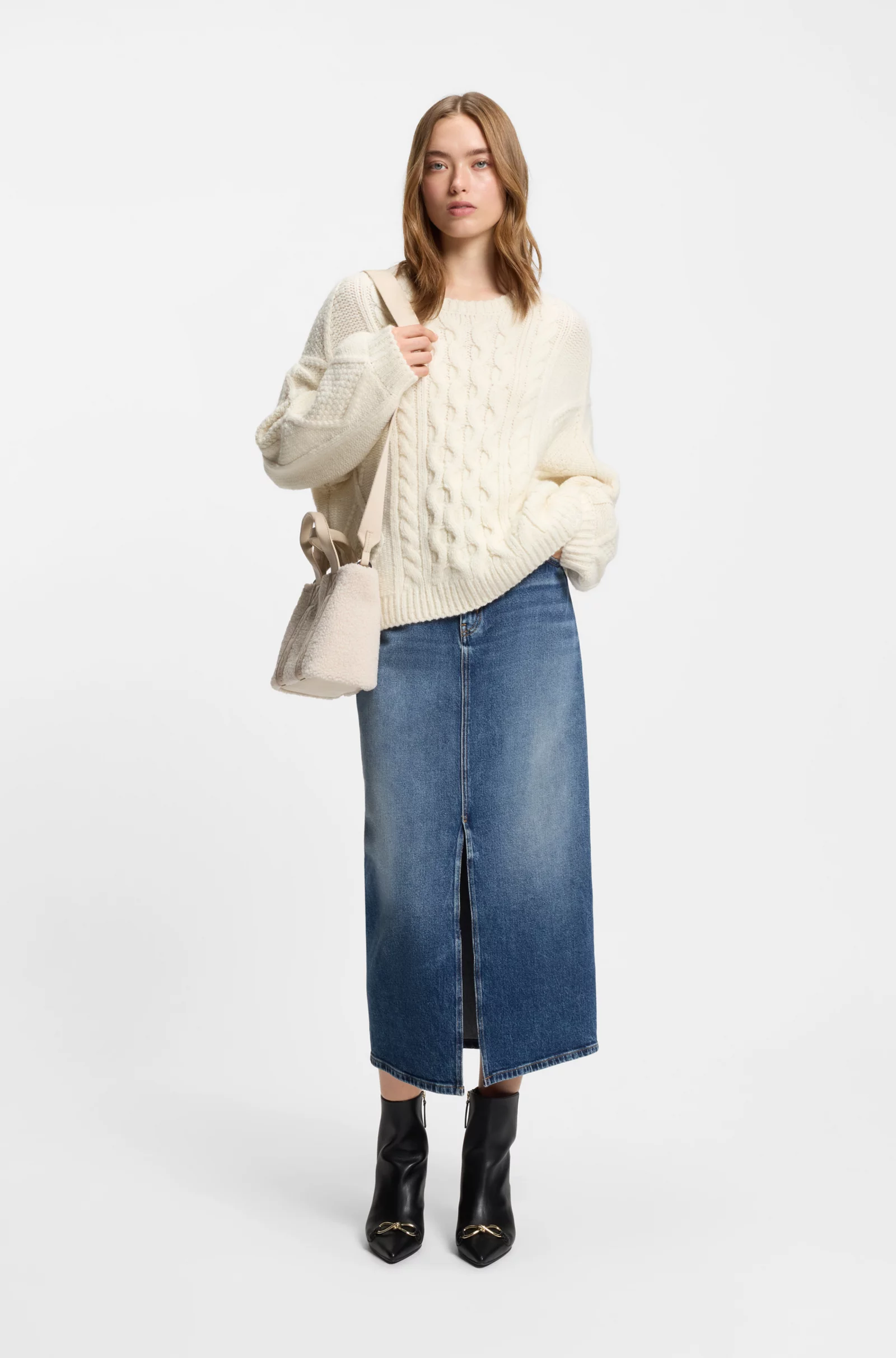 Woman wearing a denim midi skirt with a chunky cream sweater