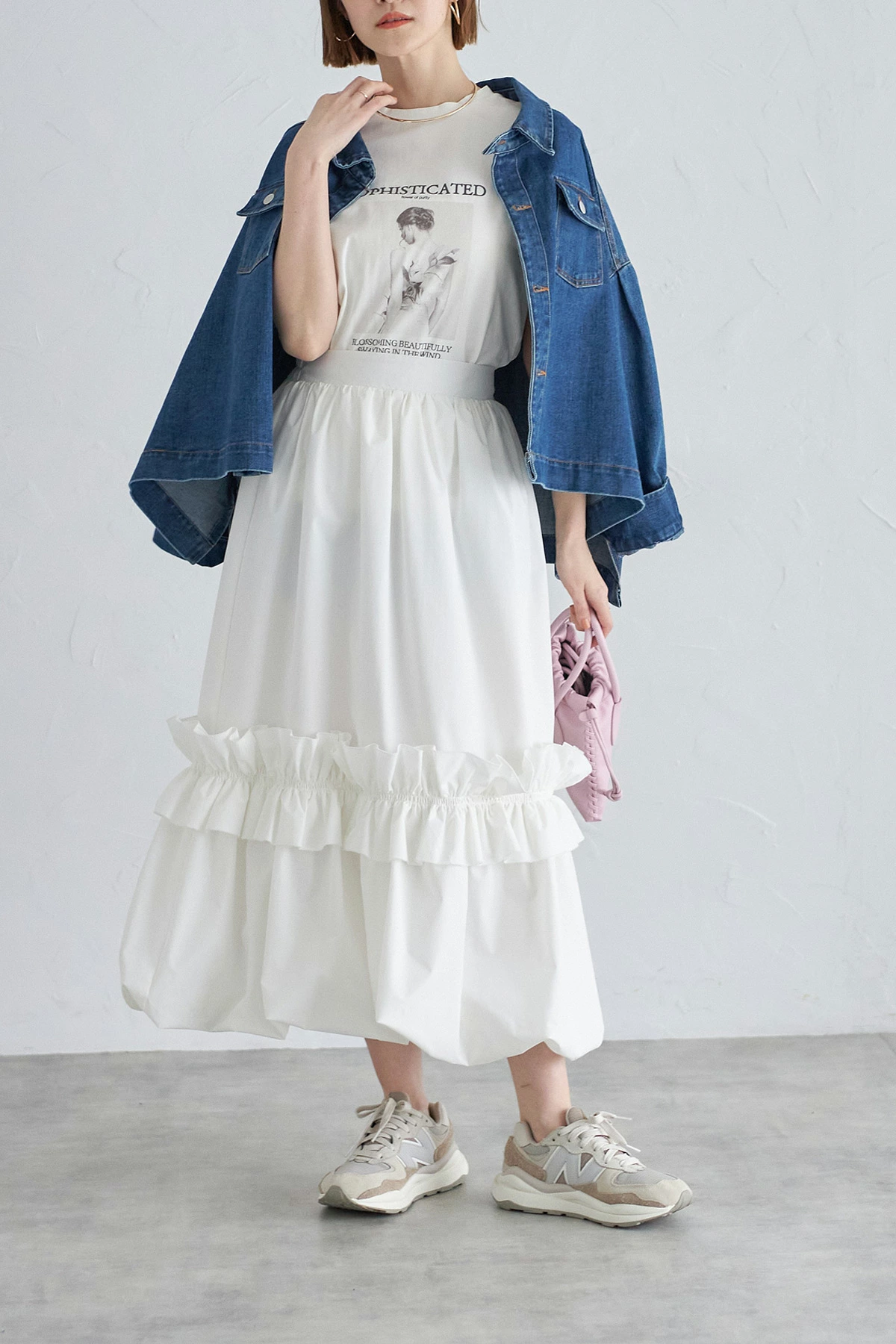 Woman wearing a tiered midi skirt with a denim jacket and sneakers