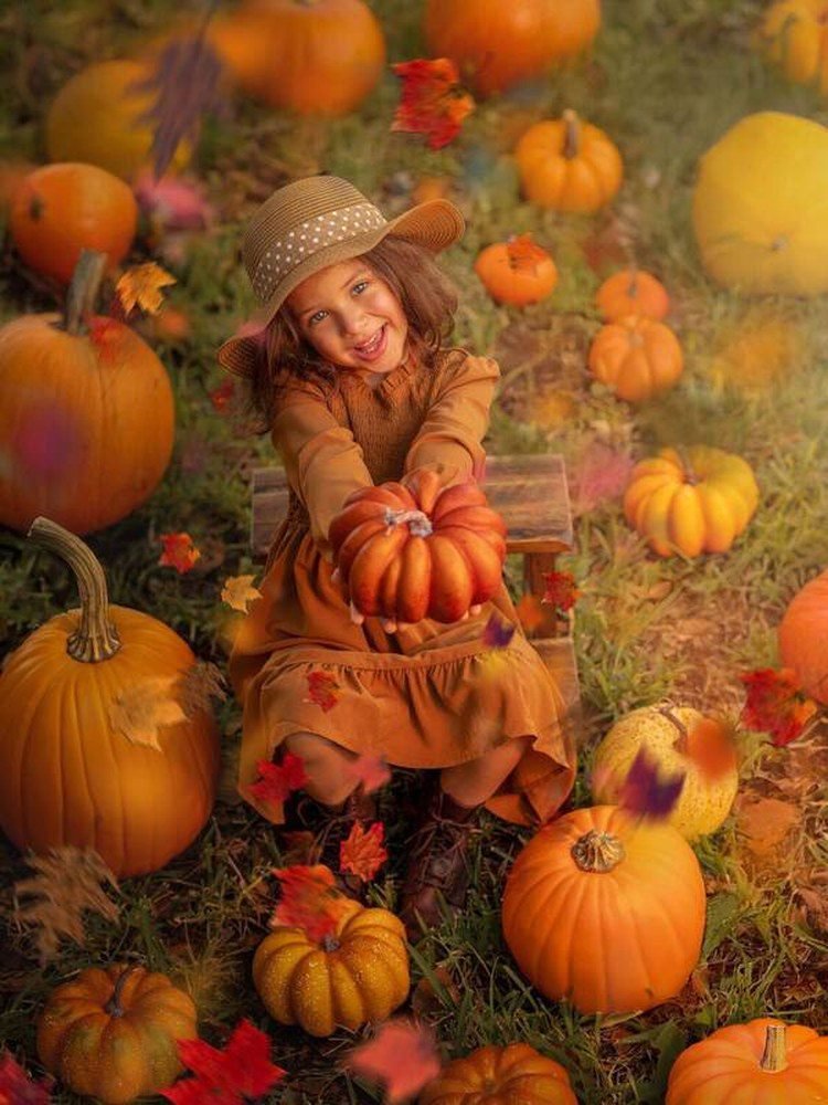 Woman standing tall among pumpkins wearing long cardigan and wide brim hat