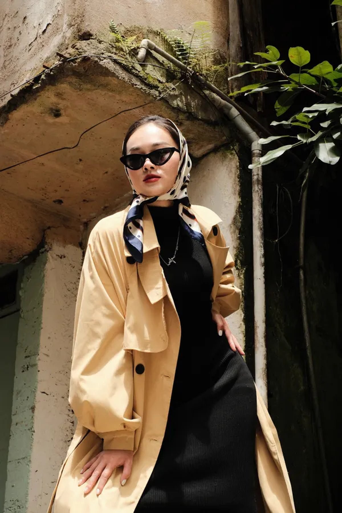 Woman styling a silk scarf as a headscarf with a trench coat