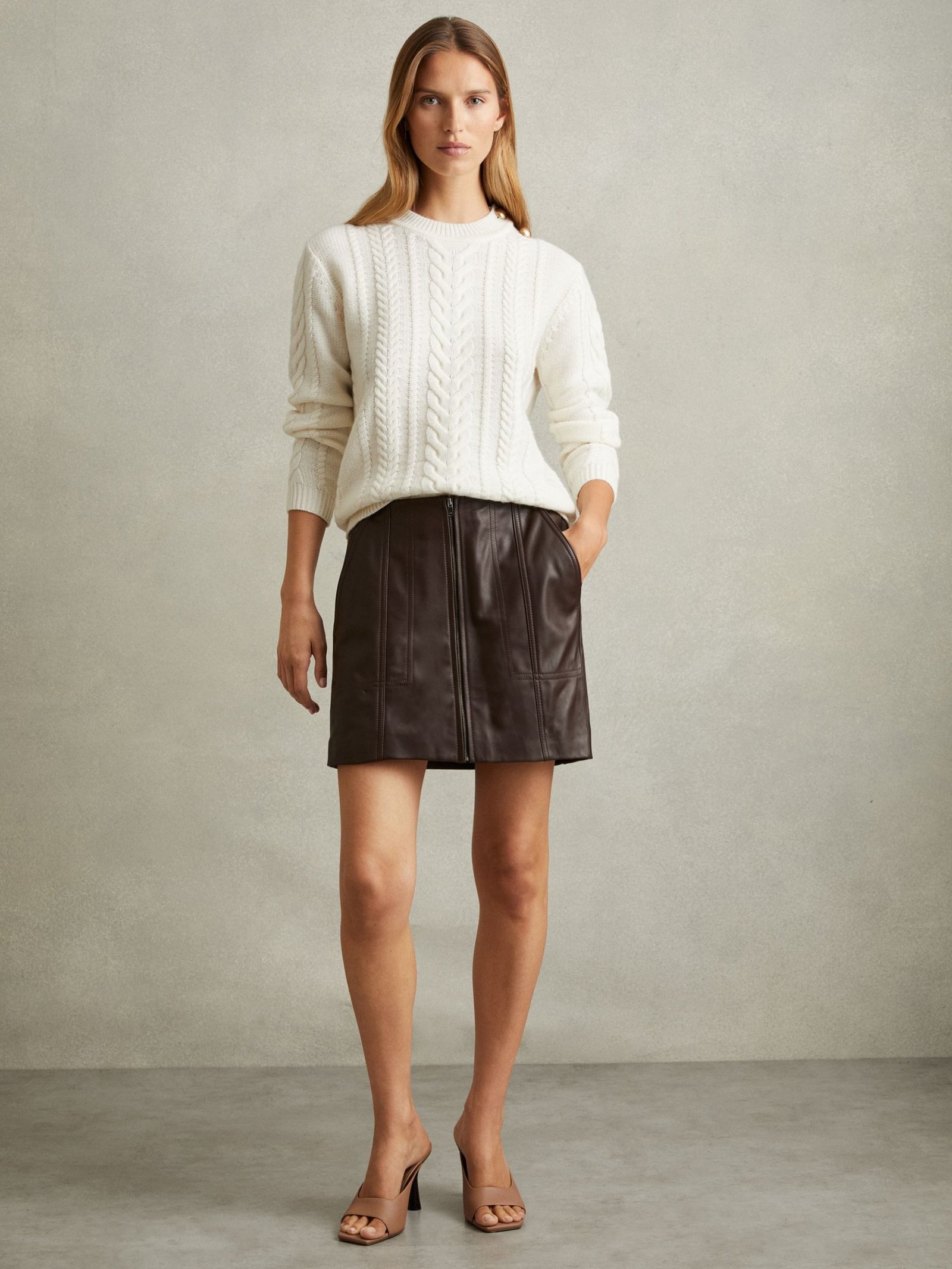 Woman in a cream cable knit sweater and leather skirt