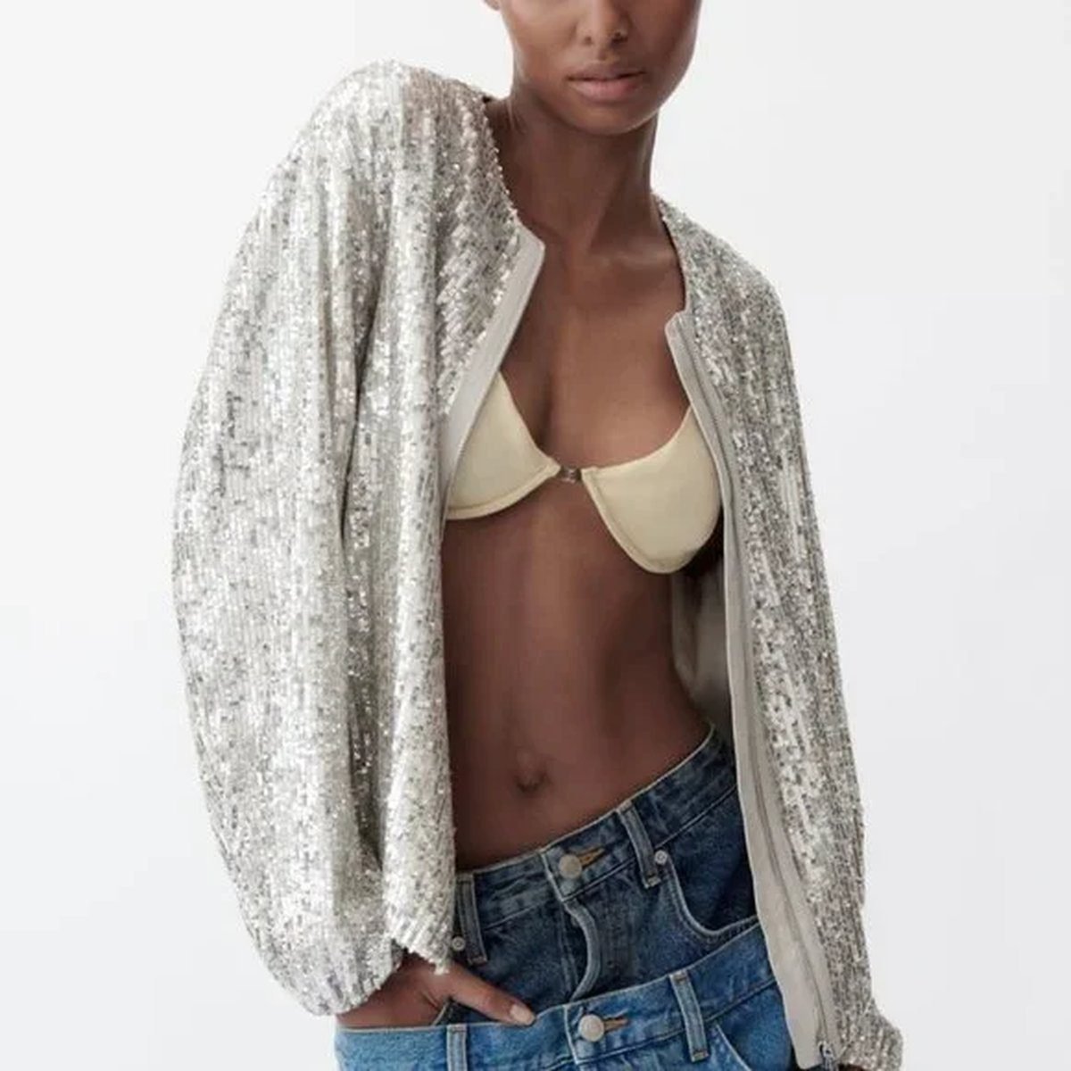 Woman in a sequin camisole layered under an open cardigan with jeans