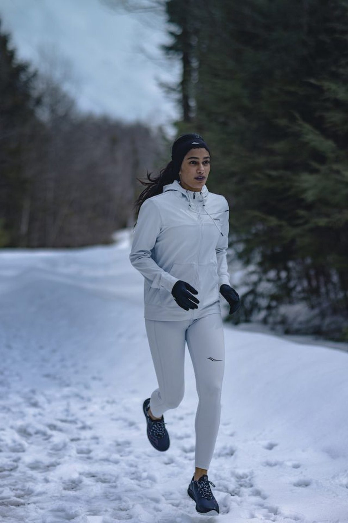 Woman running in a hooded running jacket with leggings in cold weather
